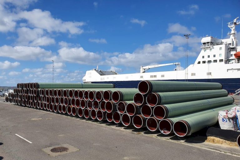 Many large sized pau wrap protected pipes stacked in port for boat shipment